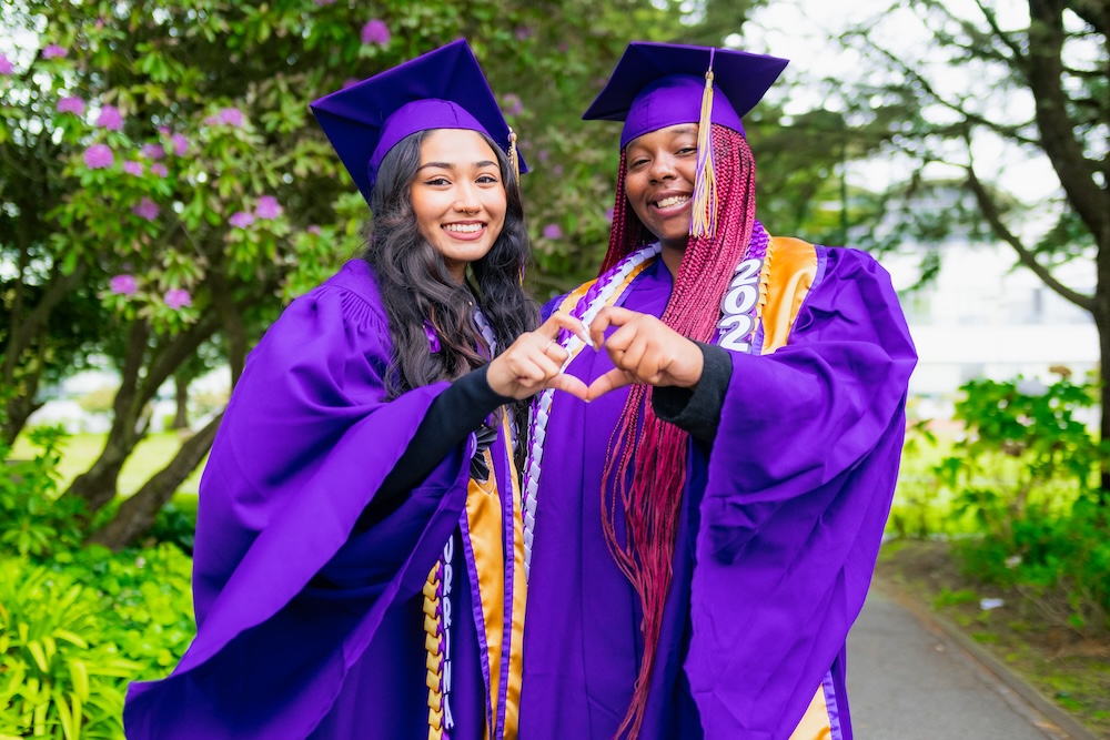 Two female students smiling wearing their purple cap and gown for graduation